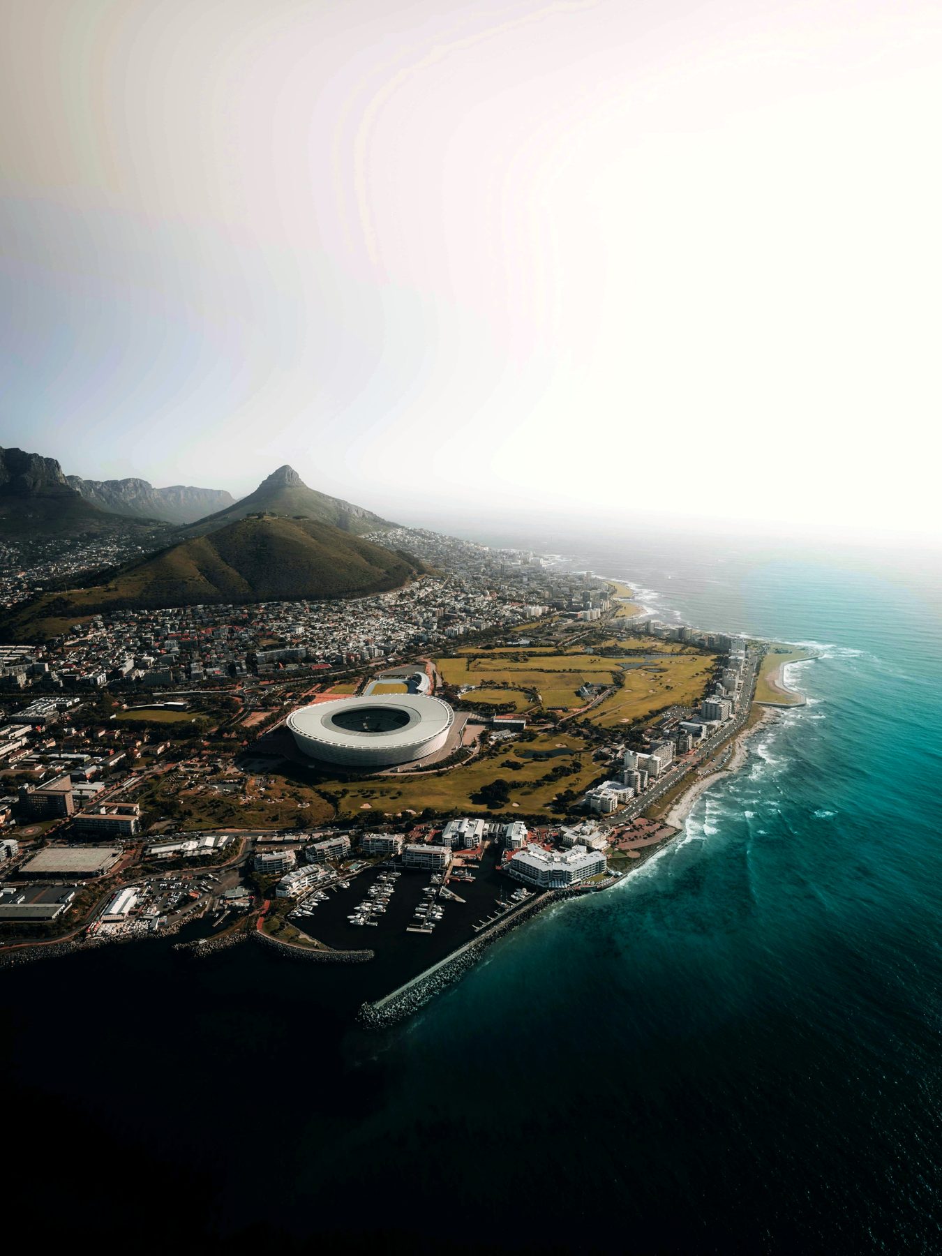 Aerial over Green Point and Three Anchor Bay on Cape Town's Atlantic Seaboard - Cape Town Stadium, Signal Hill and the ocean in frame